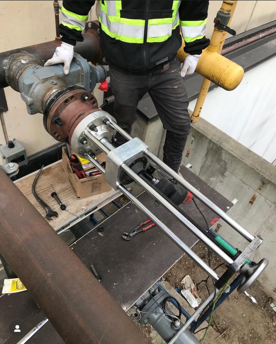 Technician operating a hot tapping machine clamped to a large-diameter live gas line