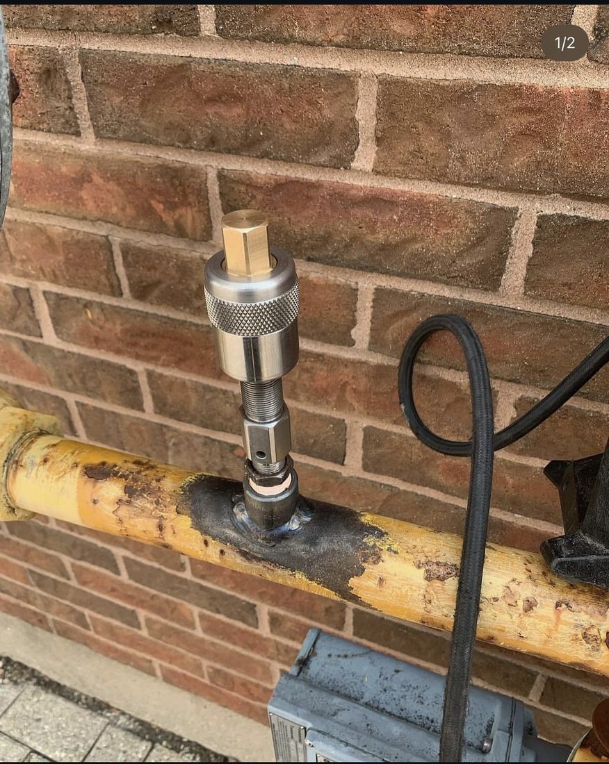 Hot tap in progress on a live yellow natural gas main running along an exterior brick wall