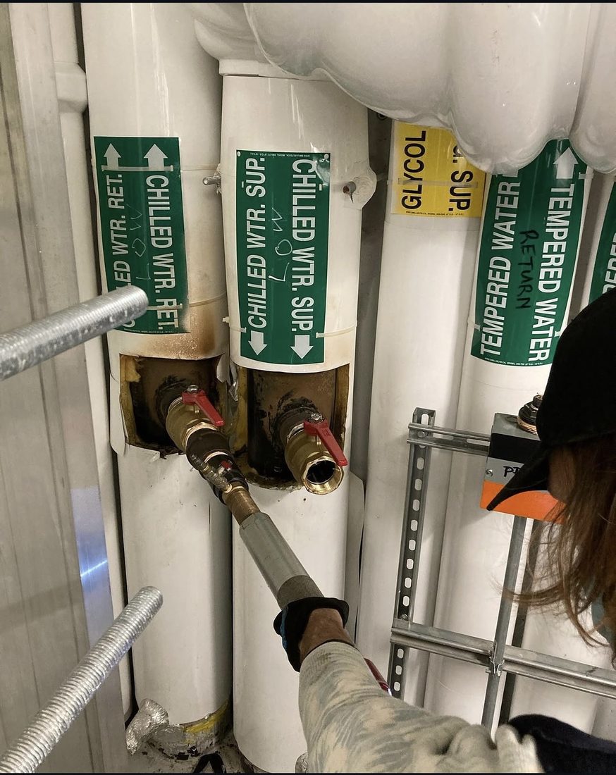 Hot tap being made into labelled chilled water supply and return piping in a mechanical room