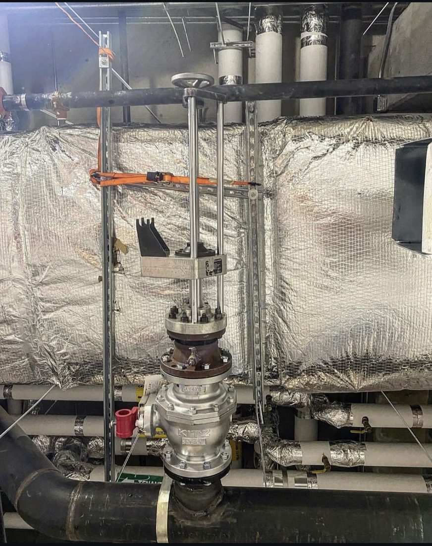 Hot tapping machine mounted on a gate valve and hot tap fitting, cutting into a live black steel line in a mechanical room